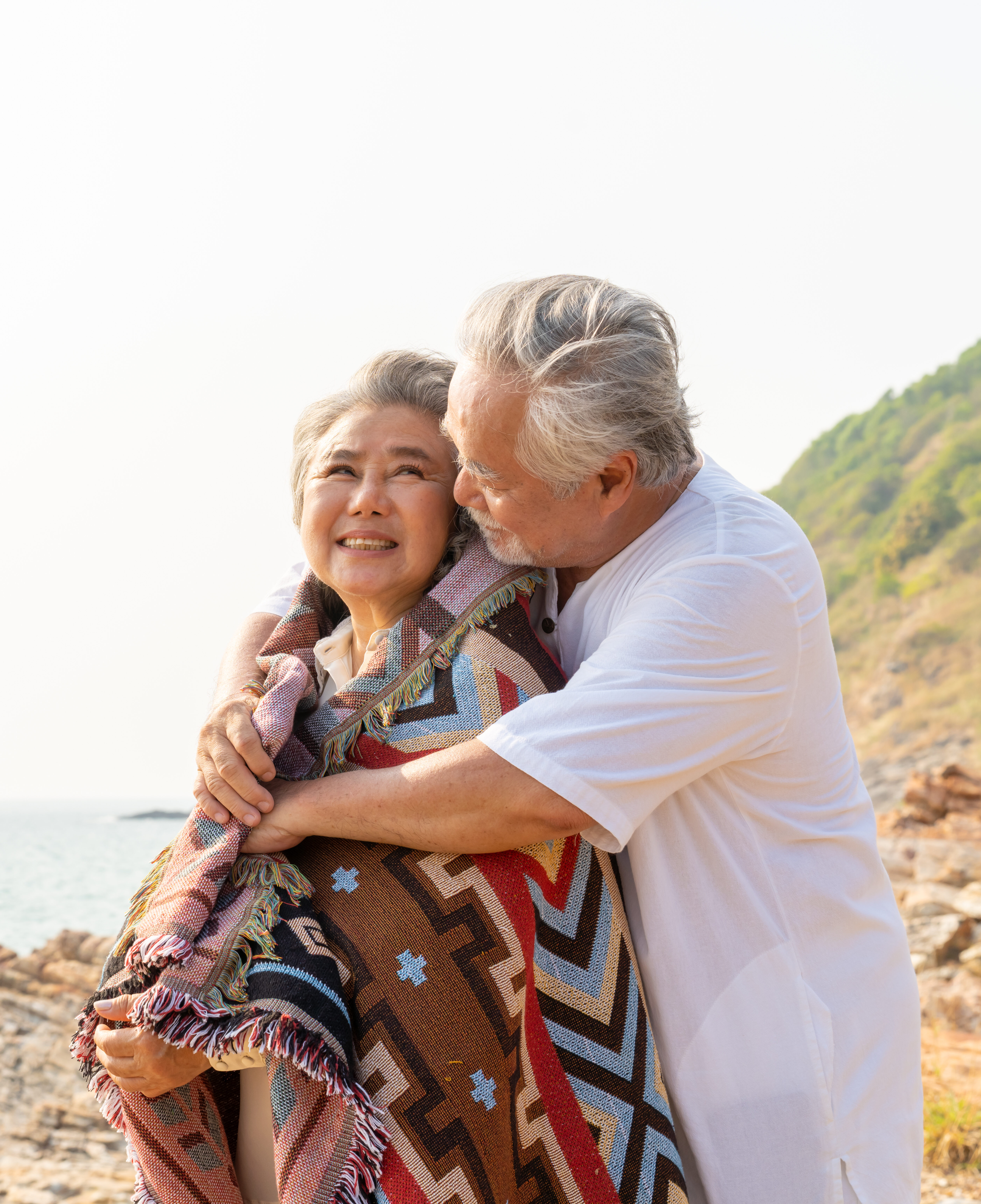 Asian family senior couple hugging each other on coastline beach at sunset. Retirement elderly people enjoy outdoor lifestyle travel ocean on summer vacation. Old person mental health care concept. asian couple 633889822 e1744228688827